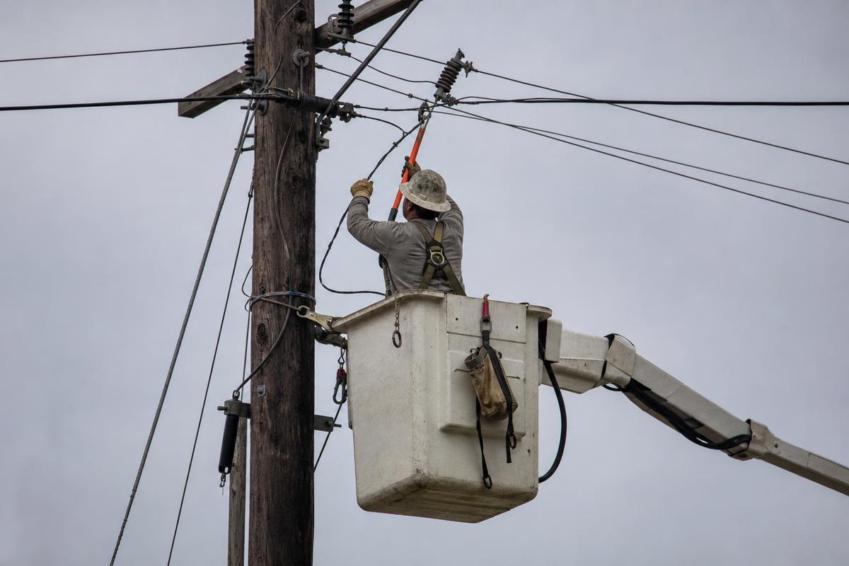 Lineman working on high-voltage transmission lines at sunset.